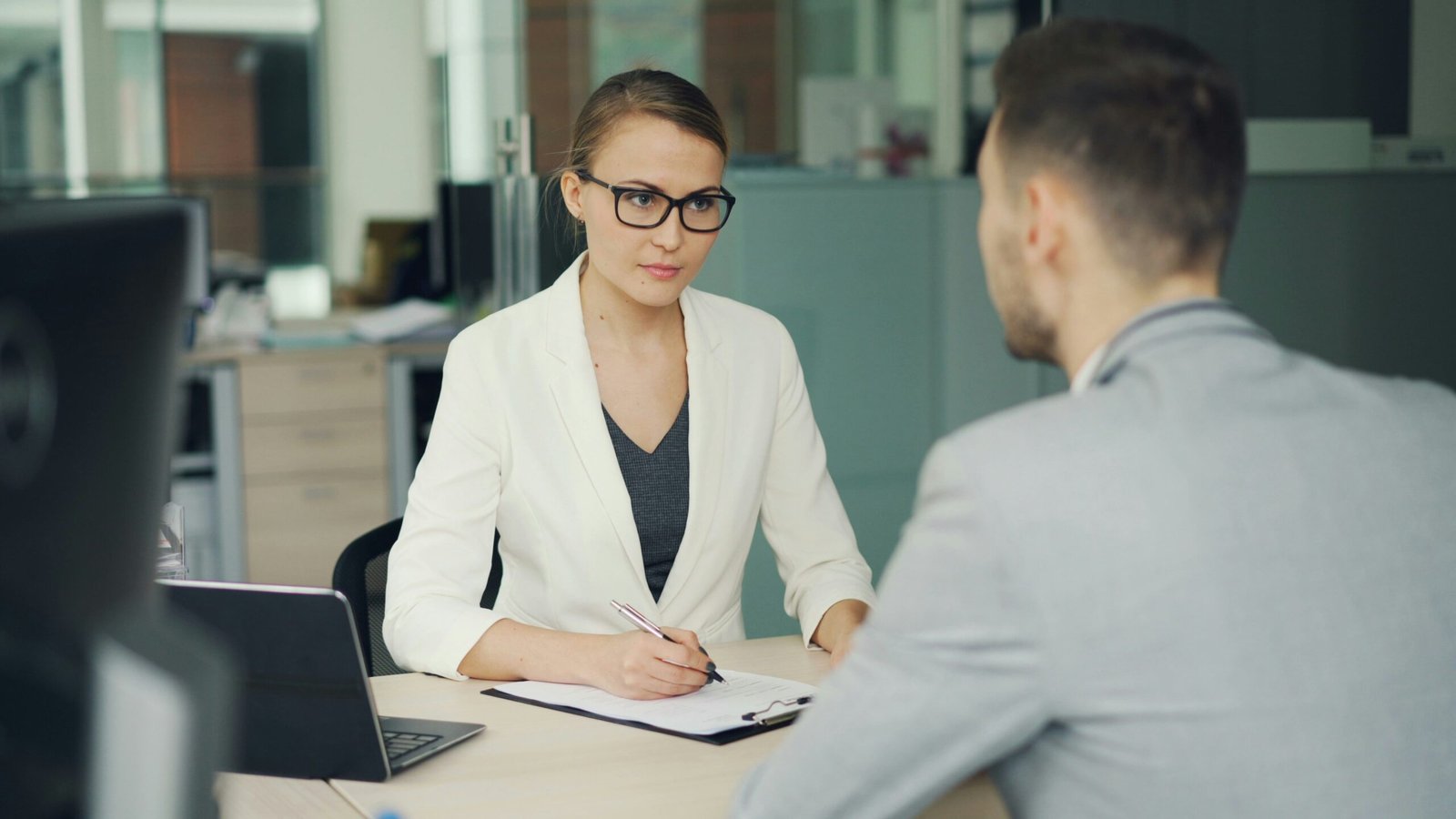 A woman in an office listens carefully while speaking with a colleague across a desk