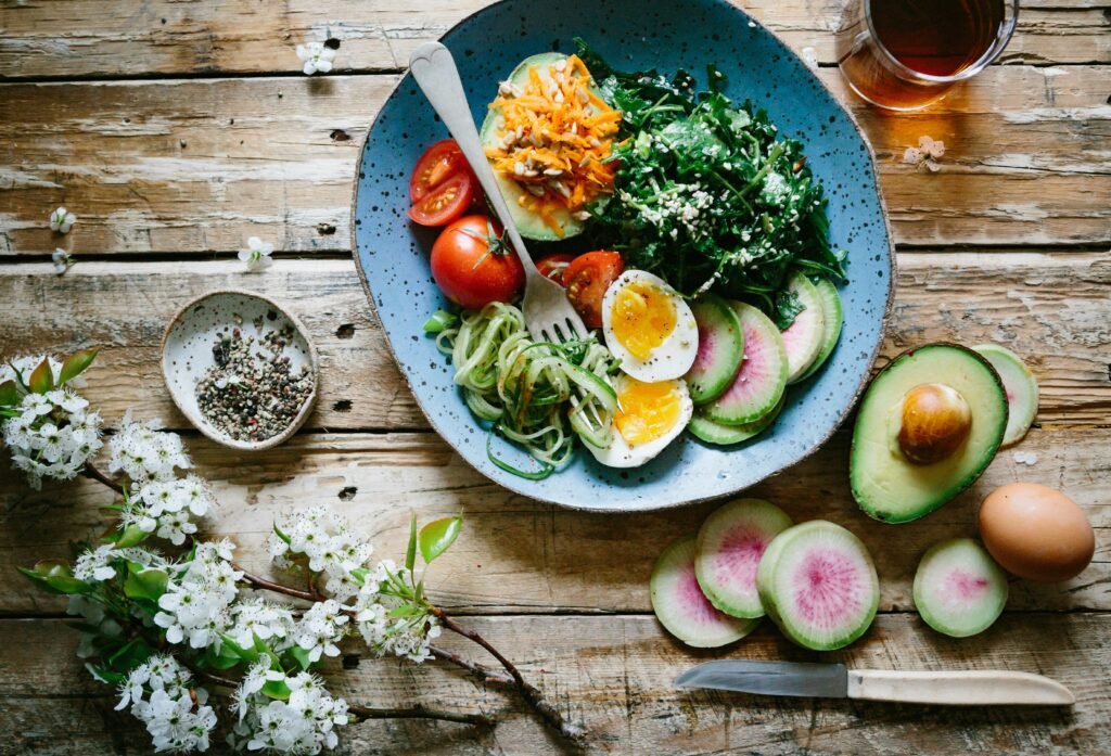 A healthy bowl of vegetables, eggs, and greens on a wooden table