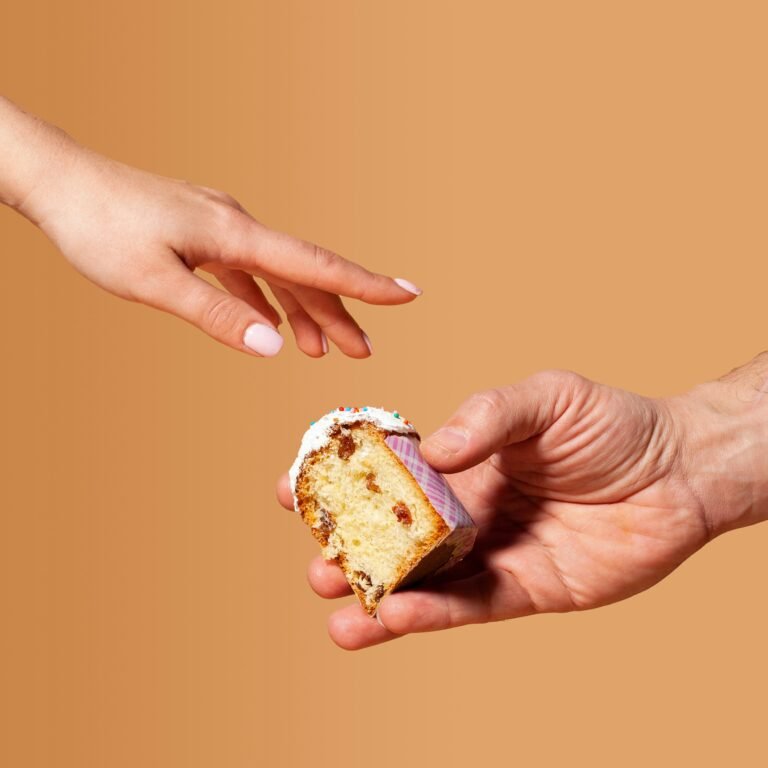 Two hands sharing a small piece of cake against a plain background