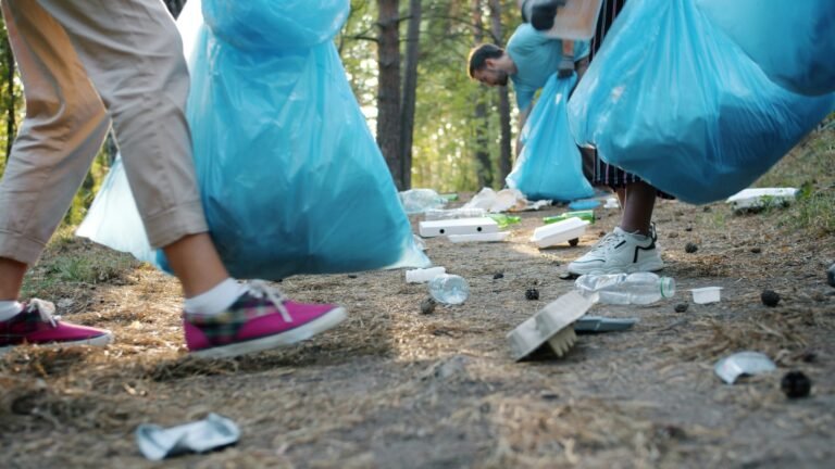 People picking up trash in a forest while holding large blue garbage bags