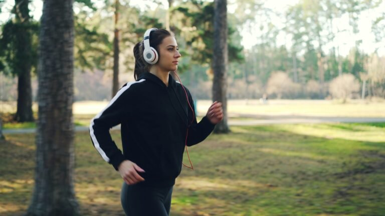 A woman jogging outdoors in a park while wearing headphones