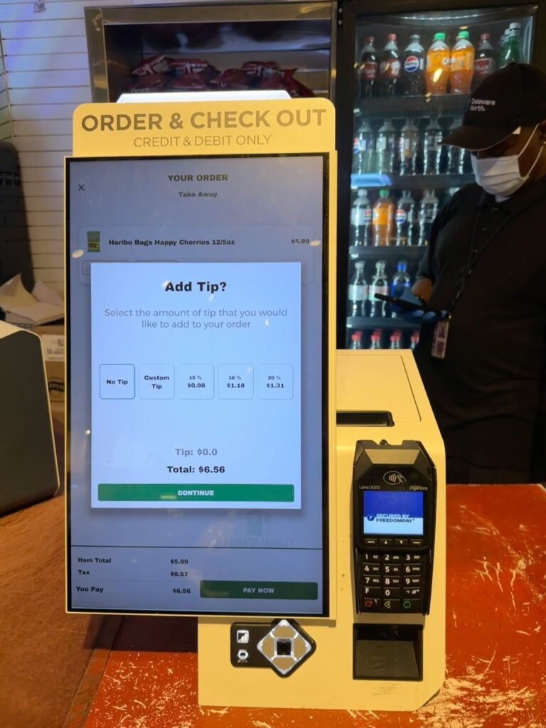 A self-checkout screen asking customers to add a tip while paying for a purchase, highlighting the growing trend of digital tipping prompts.