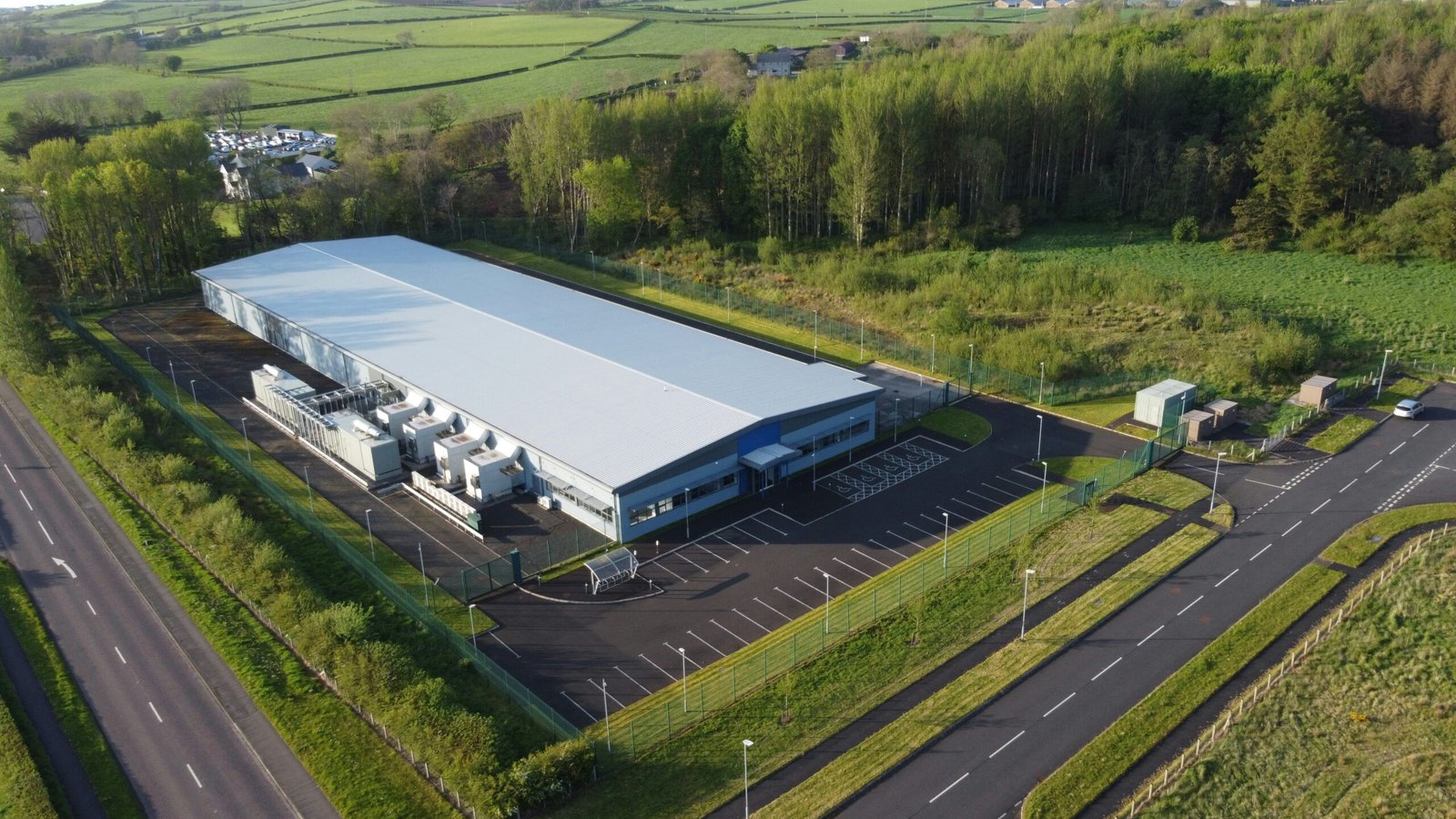 Large modern data center building surrounded by roads, trees, and green countryside viewed from above.
