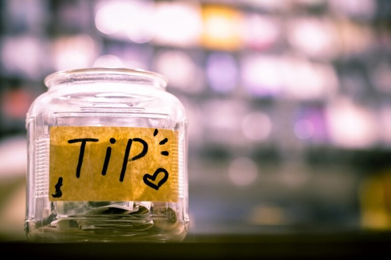 A glass tip jar with a handwritten “TIP” sign sitting on a counter, representing tipping culture and service workers.