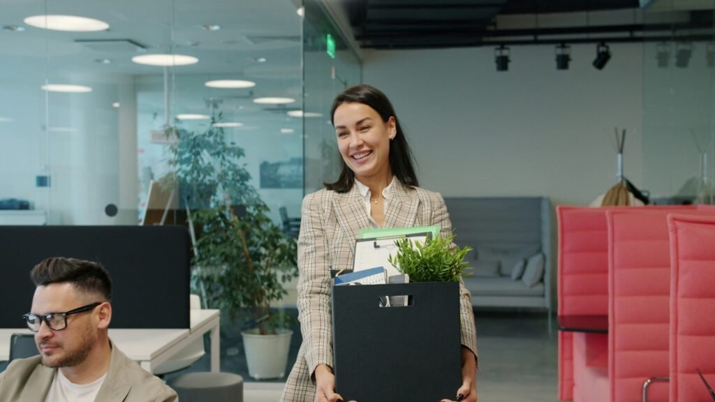 Professional woman carrying a box of office belongings as she leaves her workplace to begin a new career opportunity.
