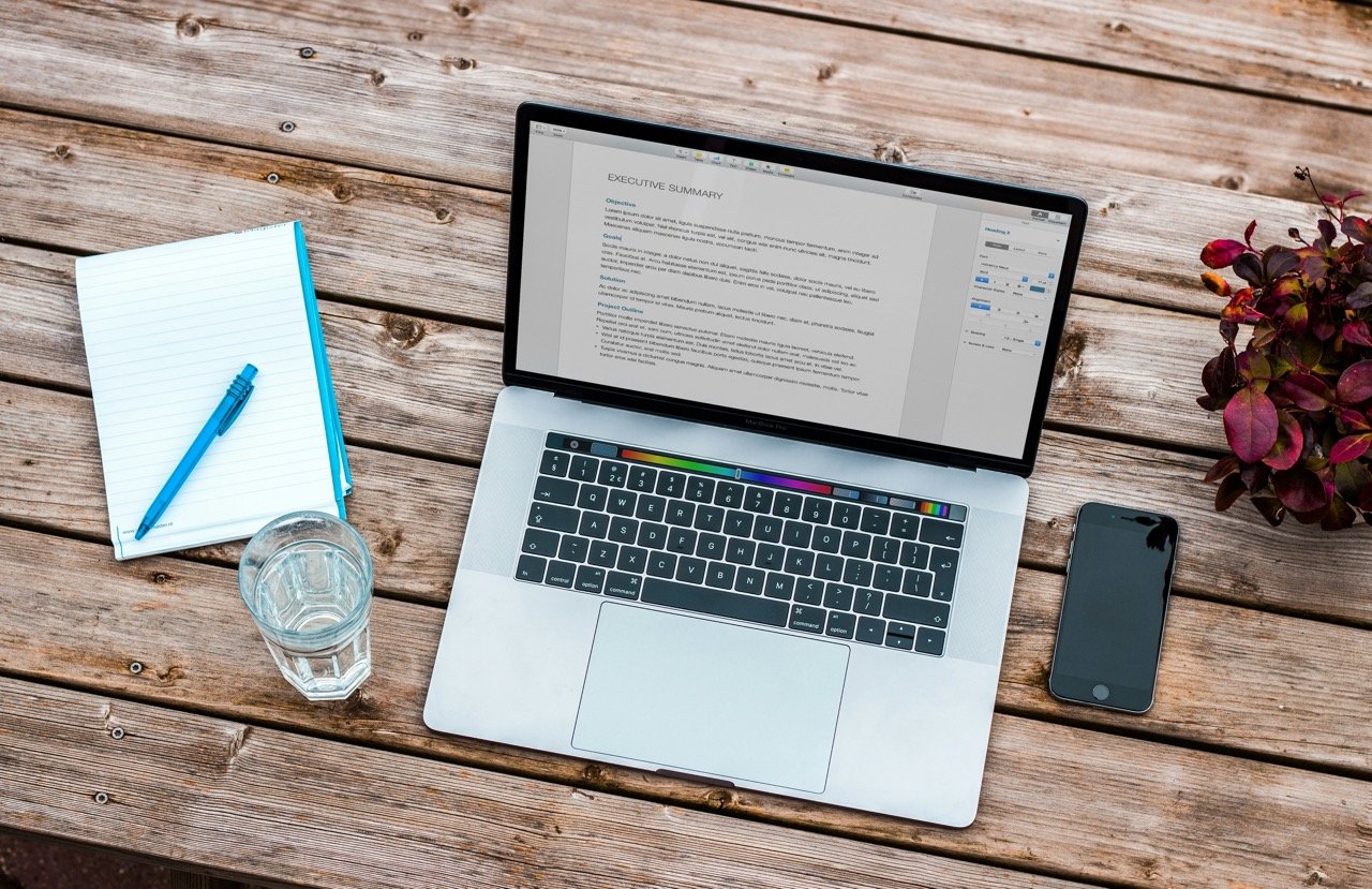 Laptop displaying a professional resume beside a notebook, pen, and smartphone on a wooden desk.