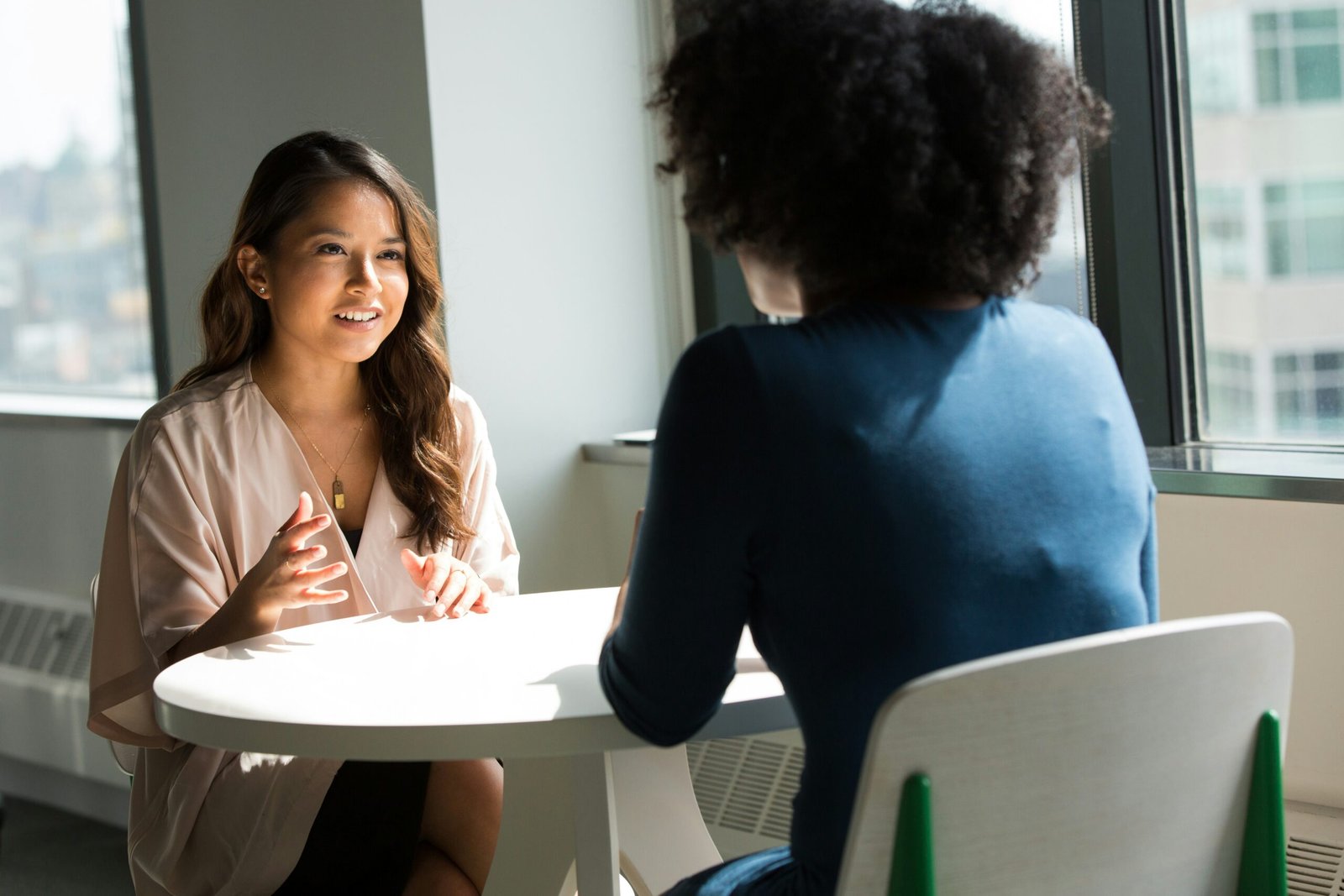 Two women having a friendly conversation at a table, illustrating English small talk and the phrase "How are you?"