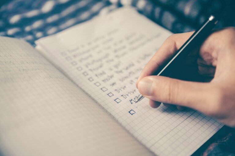 Person writing a checklist in a notebook to reflect on personal goals and priorities.