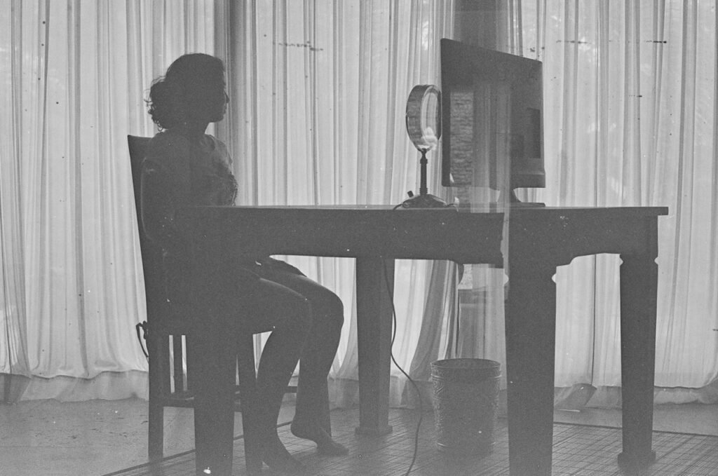 A silhouetted woman sitting alone at a desk facing a computer screen and ring light, evoking the solitary nature of talking to an AI companion