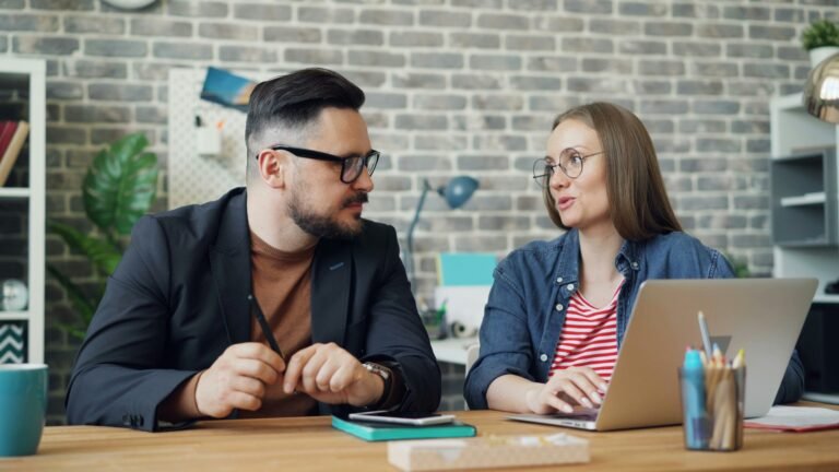 Two coworkers having a tense conversation at a desk.