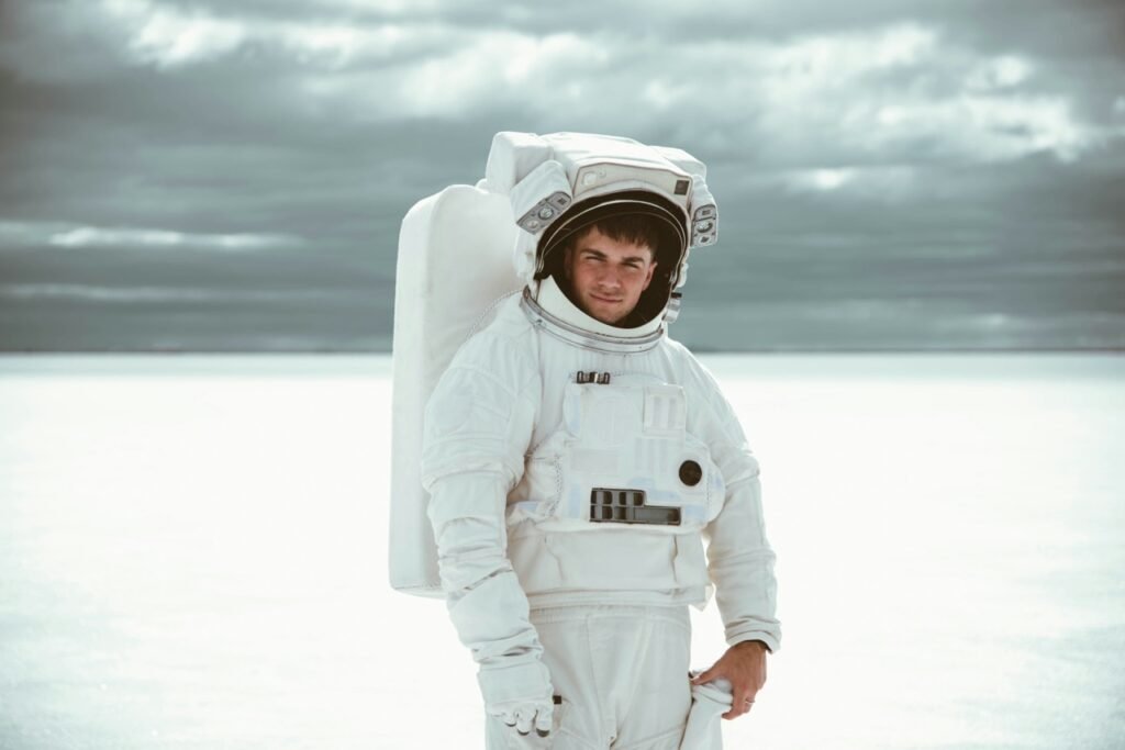 Man wearing a full astronaut spacesuit standing on a white salt flat under a cloudy sky