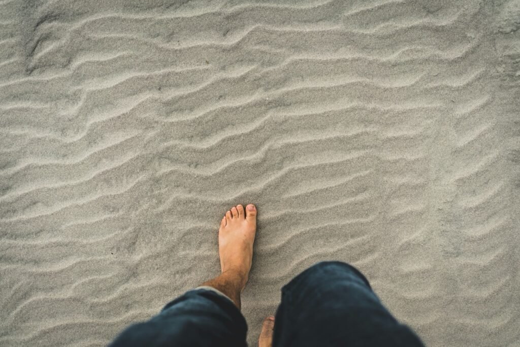 A bare foot stepping onto rippled beach sand while walking barefoot outside