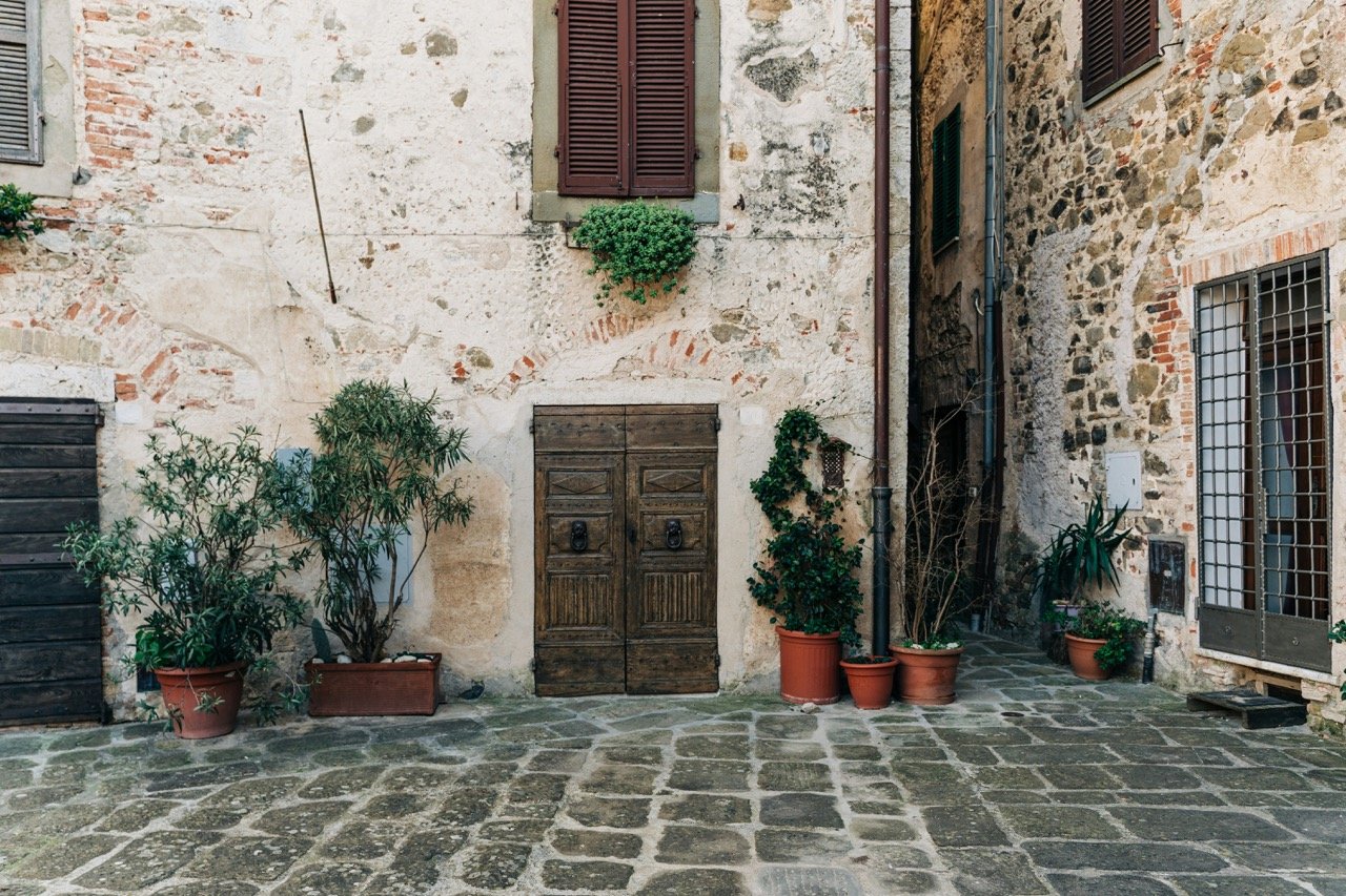 Cobblestone courtyard of an old Italian village with a rustic stone building, wooden door, and potted plants, an example of slow travel destinations