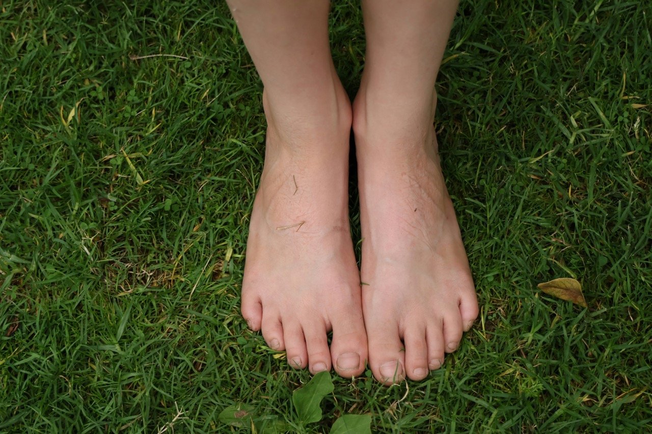 Two bare feet standing together on green grass, an example of grounding or earthing