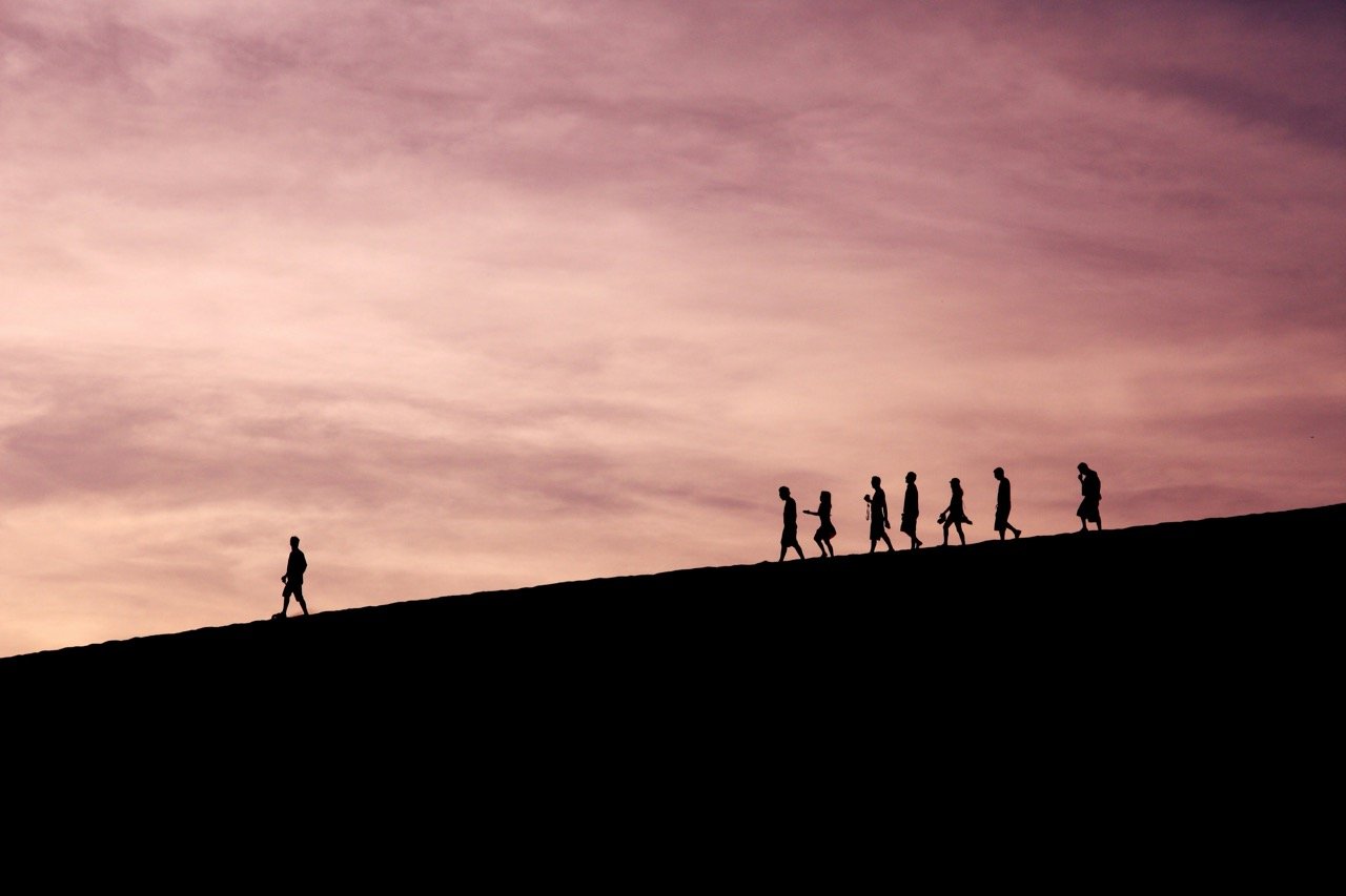 Silhouettes of people walking together along a hill at sunset with natural leader in front