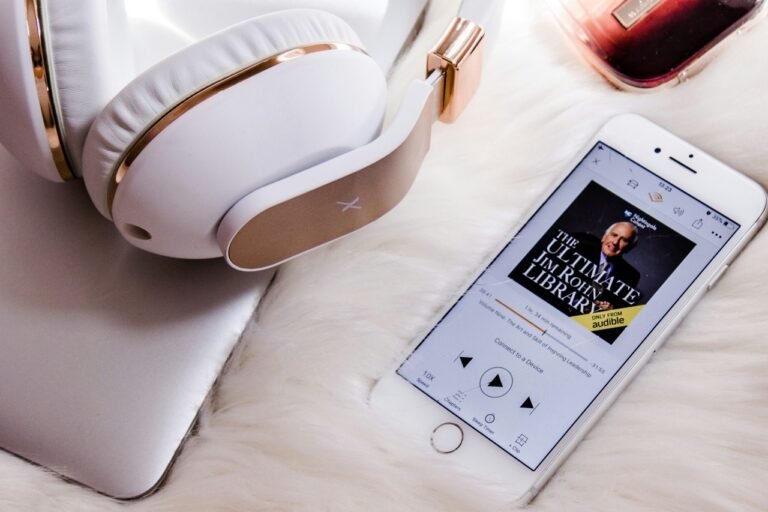 Wireless earbuds on a phone showing "Good to Great," resting on a stack of books including "Emotional Intelligence"