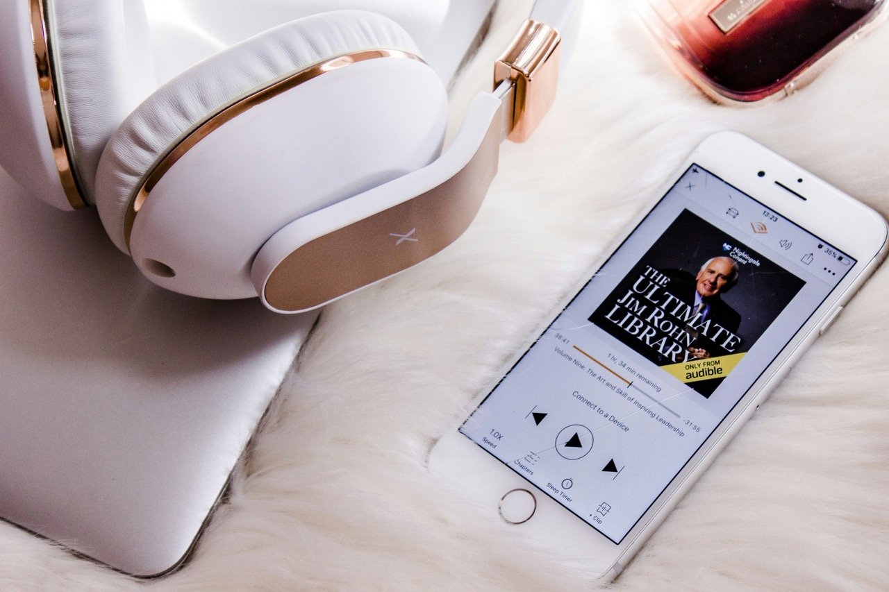 Wireless earbuds on a phone showing "Good to Great," resting on a stack of books including "Emotional Intelligence"