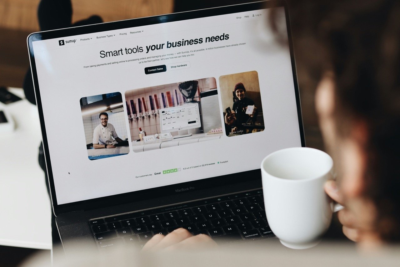 Person browsing business tools on a laptop while holding a coffee cup