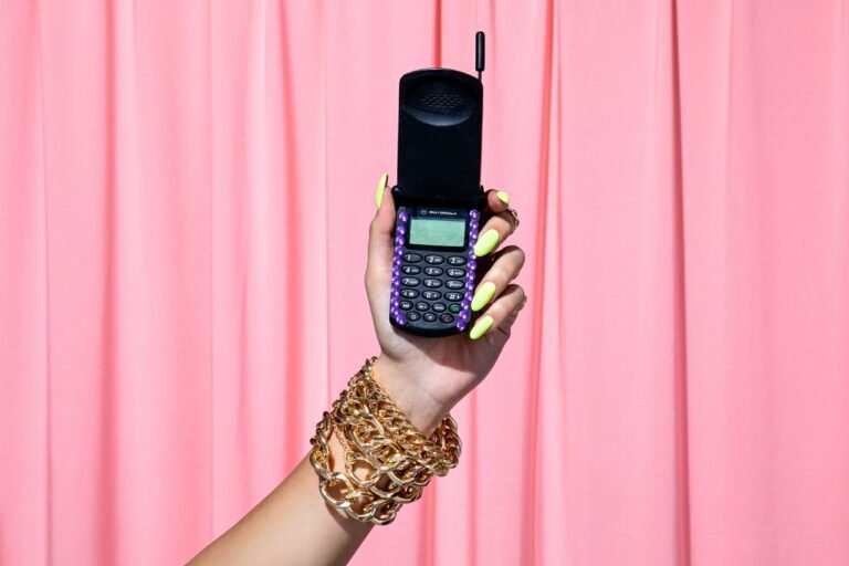 Hand holding a vintage flip phone against a pink background, representing the growing trend of switching from smartphones to dumbphones.