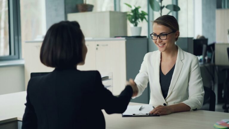 Woman shaking hands with a job interviewer across a desk during a meeting