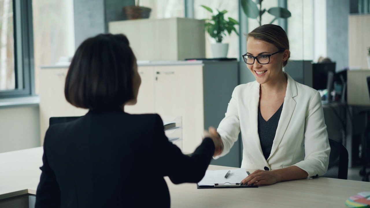 Woman shaking hands with a job interviewer across a desk during a meeting