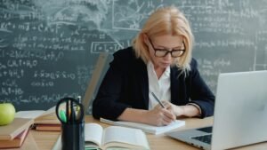 Teacher planning a lesson with books, notes, and a laptop at a classroom desk