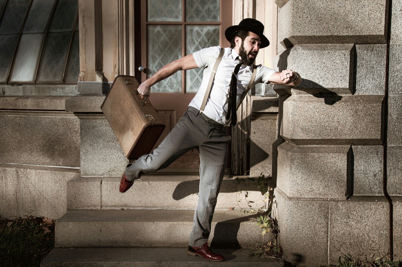 Man in a hat checking his watch while rushing down stone steps with a briefcase, illustrating the importance of punctuality.